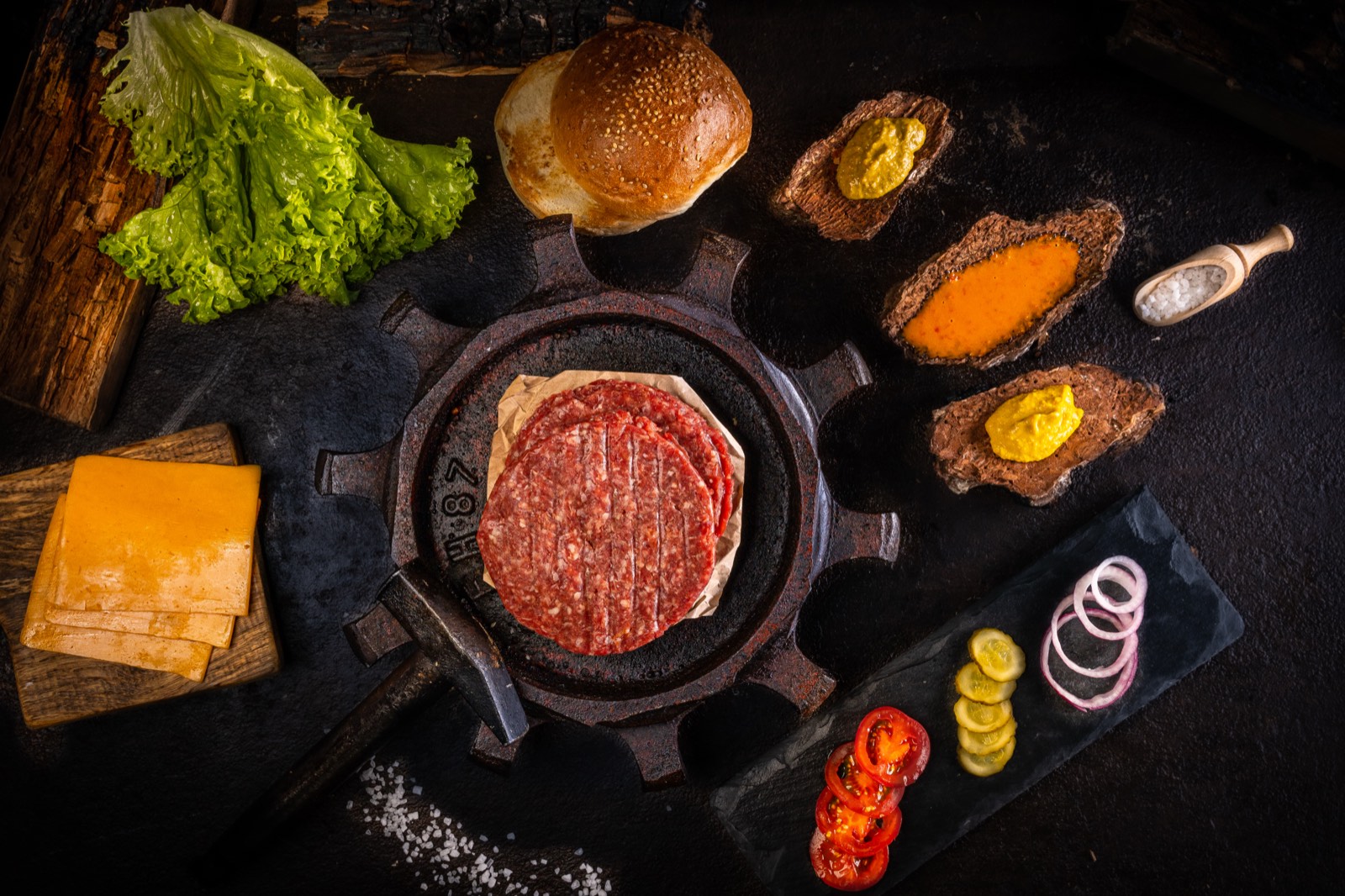 Zutaten für einen Burger: Hackfleisch-Patty in der Pfanne, Brötchen, Salat, Käse und Soßen